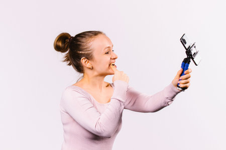 Caucasian girl blogger makes faces and takes selfies for her followers. White background and time...