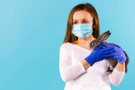 Happy Pandemic 2021 Easter. Young caucasian woman wearing medical blue gloves and mask holding a...