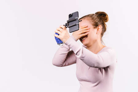 A young blonde during a straight transmission laughs and covers her eyes with her hand. Smartphone and blogging concept.の写真素材