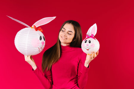 Caucasian girl smiling and posing with handmade decorative rabbits. Reds background and Easter...