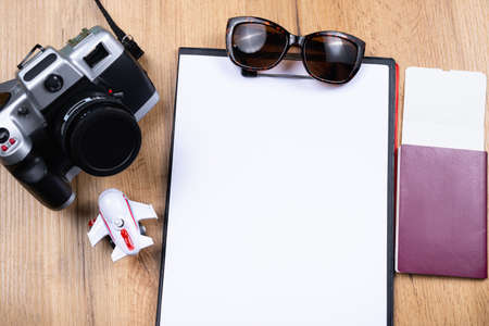 Tourism and travel concept. White empty folder sheet, passport with flying ticket, passenger plane figurine, sunglasses and vintage camera on wooden table background. Top view.の写真素材