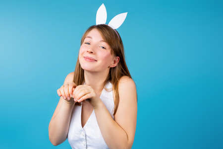 Cute young girl with easter bunny ears posing on blue background with empty side space. Funny girl dressed as a rabbit for Easter holidays. High quality photoの写真素材