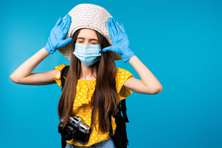 Woman tourist in summer clothes, hat, camera and medical mask and gloves on a blue background....