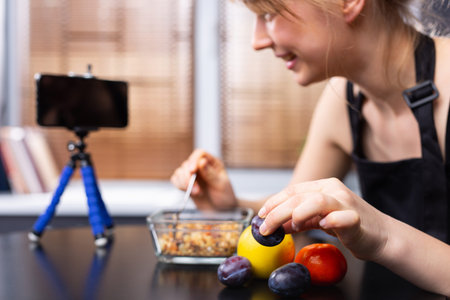 An enlarged photo of a food blogger girl in front of the phone camera with cereals and fruits on a blurred background. The concept of stream blogging and proper nutrition. High quality photoの写真素材