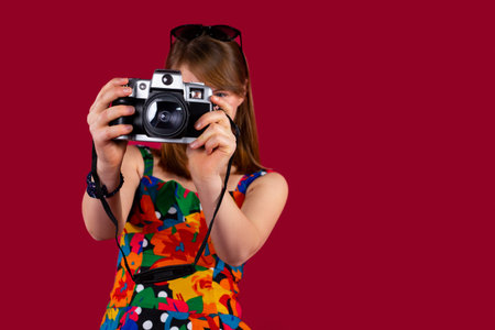 A blonde girl with sunglasses on her head and in bright colorful blouse is taking pictures with a...