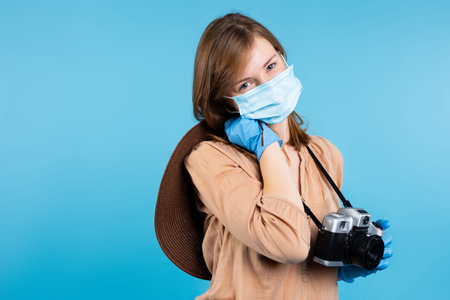 Portrait of a girl journalist with a camera in a summer hat, protective gloves and a medical mask...