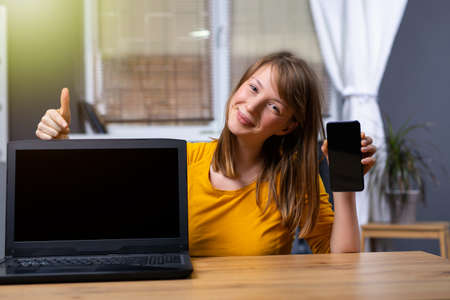 The woman uses a laptop and a smartphone with a blank black screen at home. Template for your look. Black mock up gadgets screen. High quality photoの写真素材