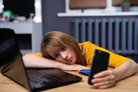 Overworked tired woman. Young exhausted student girl sleeping in office. Woman using laptop, smartphone at home office. Entrepreneur, business, freelance work, study, stress. High quality photoの写真素材