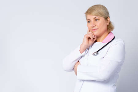 Thoughtful senior female doctor, lost in thoughts. Worried old physician thinking of healthcare question, concerned of challenge, feels anxious, difficult decision. Side space. High quality photoの写真素材