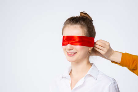 Surprised excited woman closed her eyes with red ribbon waiting for a surprise, isolated on white background with empty space. High quality photoの写真素材