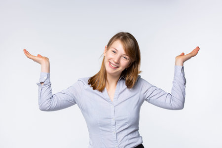 Studio portrait of a happy young blonde, raising her hands in a gesture of uncertainty, shrugging,...