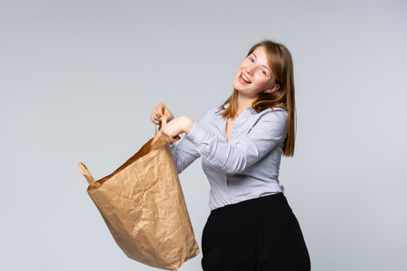 Charming young and cheerful blonde woman holds a eco package , showing forefinger inside. Wearing...
