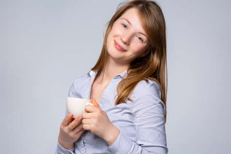 Portrait Caucasian women on gray studio background. Beautiful and smiling female model in white shirt. The concept of human emotions, facial expression, sales, business woman. High quality photoの写真素材