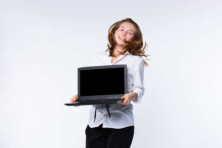 Online business concept. Smiling caucasian young woman, jumping on gray background, holding black mock up laptop, recommend download app, consultation application. High quality photoの写真素材