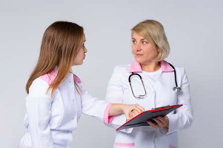 Amazed, shocked, dizzy medical doctors are discussing diagnosis during the conference pointing in sheet folder. Successful healthcare workers on gray background. High quality photoの写真素材