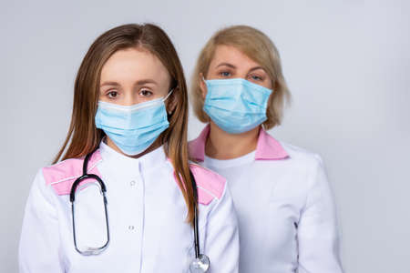 Health, medicine and pandemic concept - close up of two caucasian female doctors or scientists in protective mask, medical workers at hospital on gray background. High quality photoの写真素材