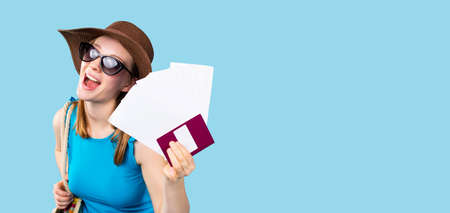 Banner, long format. A tourist with a smile looks at the camera in summer clothes and a hat holding tickets and a passport. Side space for text and advertisements. High quality photoの写真素材
