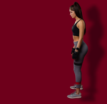 Full length, assertive woman gymnast with shadow in sportswear with two elastic band on knees,...