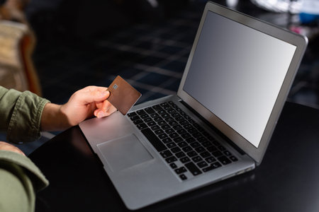 Cropped photo of hands of man using laptop at home, holding credit card, online home shopping,...