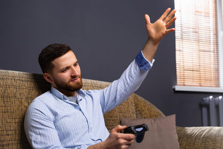 A man at home sitting on the couch with a joystick in his hands. The disgruntled man is outraged...