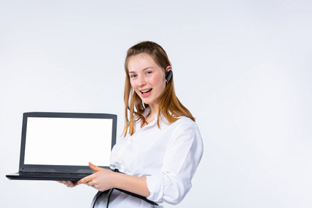 Young blonde with earphone in the ear. Shows a white laptop screen to the camera. White background.