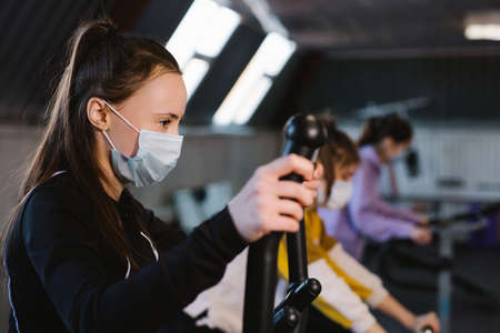 A photograph of a brunette athlete doing exercises wearing a protective mask, and in front of it are two other girls with the same training attitude. Protection concept.の写真素材