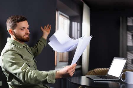 A tired disgruntled caucasian man scatters documents at home, working remotely. Side white space.の写真素材