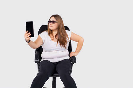 Stylish overweight young female manager having serious concentrated facial expression working distantly from home using smartphone, making business calls or listening to musicの写真素材