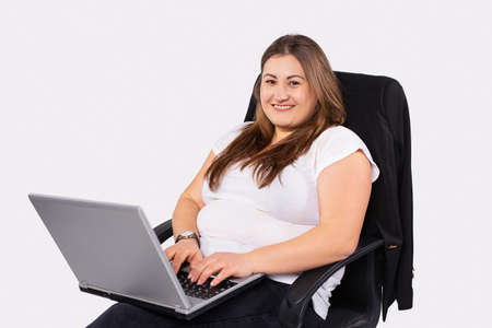 Caucasian woman working on laptop sitting in office. Overweight young woman staying at home during quarantine. Self isolation. Working distantly from home using laptop.の写真素材