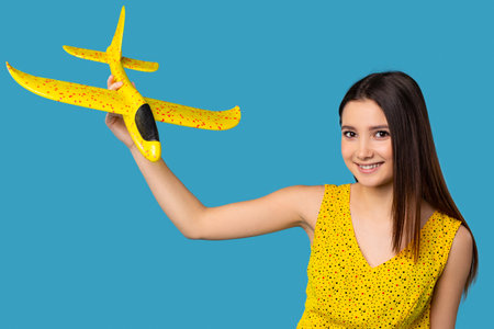 Young businesswoman holding a illuminating color airplane toy over isolated blue background, happy...