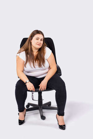 Portrait of a serious - large woman in a black leather armchair looking at the camera on a white background. Business woman.の写真素材