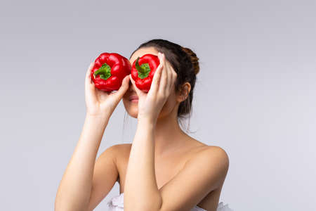 A beautifull brunette, wrapped in a towel, holds 2 bell peppers next to her eyes, promoting the concept of health, rational and balanced nutrition. Health is the slogan of life.の写真素材