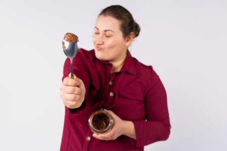 Crazy, young blonde caucasian large woman, showing spoon with chocolate cream to camera, holding...