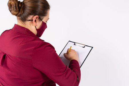 Rear photo of an overweight woman in a mask filling out paperwork. Working during a pandemic. White...