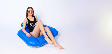 Banner,long format. A cute girl with a beautiful figure in a swimsuit and sunglasses posing in an inflatable pool. Side space for your text or advertisements.の写真素材
