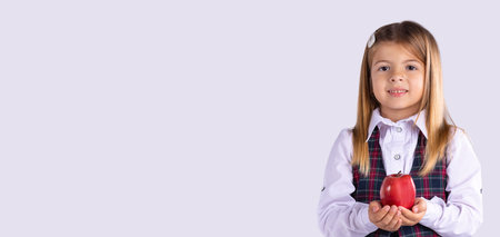 Banner, long format. A portrait of a schoolgirl girl in uniform looks at the camera with a smile and holds a red apple in her hands.の写真素材