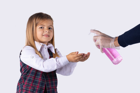 A girl in a school uniform looks at the camera smiling disinfects hands with antiseptics before entering school. Security measures during a pandemic. Grey background.の写真素材