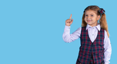Banner,long format. Caucasian girl of elementary grades in a school phonerm points up with her index finger. Blue background and space for your ad or text.の写真素材