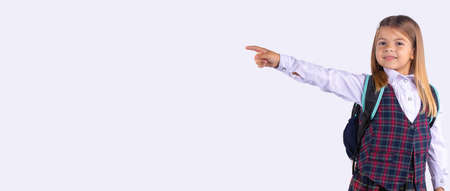 A cute caucasian girl in a school uniform looks at the camera and shows with her hand to the empty side space. Banner. Gray studio background.の写真素材