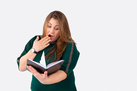Surprised young overweight woman, gesturing surprise, reading a exciting book while sitting at the...
