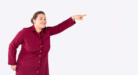 Half length shot of optimistic young caucasian large woman pointing happily into distance, observes funny trick, enjoys favourite hobby, wearing formal dress and hairstyle, spends work break activelyの写真素材