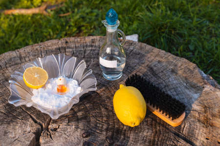 Cleaning products: baking soda with brush, clean household solution and an ampoule of essential oil, lemon on grass background, outdoor photoの写真素材