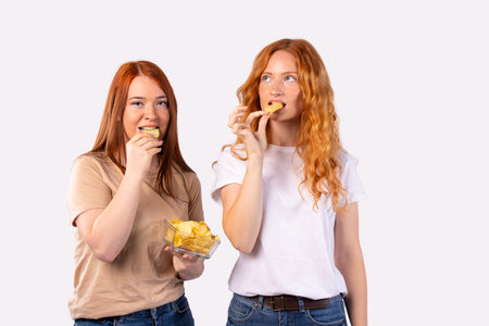 Red-haired girls eat potato chips. A quick snack on a white background with empty side space for text or advertising.の写真素材