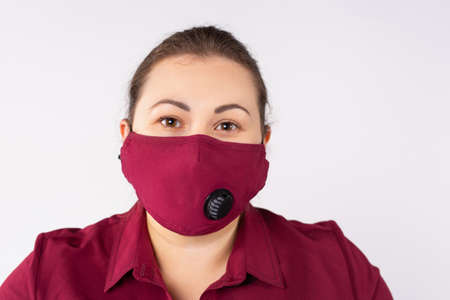 Beautiful woman in medical mask. Close-up of a young woman with a bordo surgical mask on her face against sars-cov-2. Portrait of girl listen covid-19 quarantine news. High quality photoの写真素材