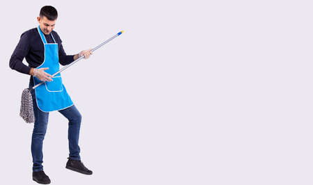 A full-length photo of a man dancing in an apron and a mop on a gray studio background with empty side space for text or advertising. High quality photoの写真素材