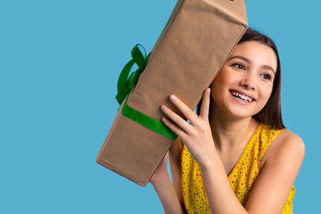 A beautiful girl is happy with the gift she received. Blue background. Gift box and holidays concept. High quality photoの写真素材