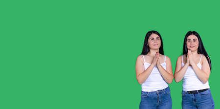 Banner, long format, green background. Smiling happy latina women saying a prayer. The caucasian twin girls looks up while praying. Plenty side space for ad promotion, sale text. High quality photoの写真素材