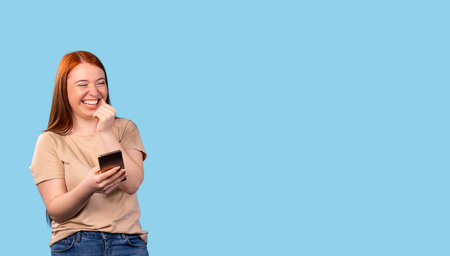 Excited red-haired cute young girl laughs on a pastel blue background with side space for ad....