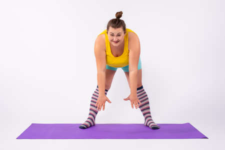 Young fat Caucasian woman bending over a sports rug. A chubby girl stretching from a distance on a yoga mat. High quality photoの写真素材