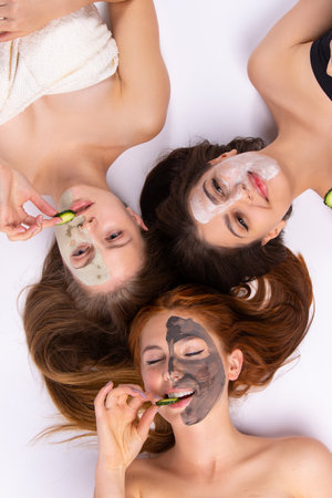 Home spa. Three women holding pieces of cucumber on their face lying down. Beauty salon concept, health. High quality photoの写真素材